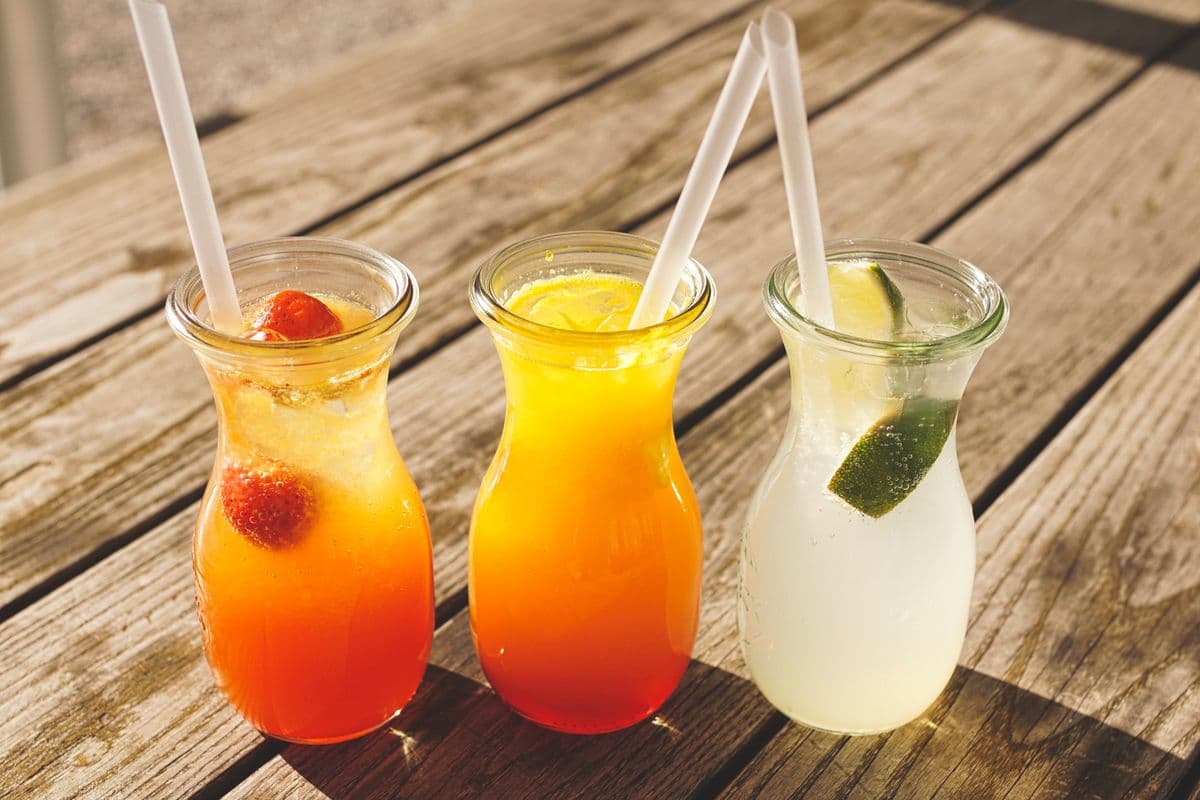 Three carafes of fresh-pressed juice in red, orange and citrus tones on a wooden table