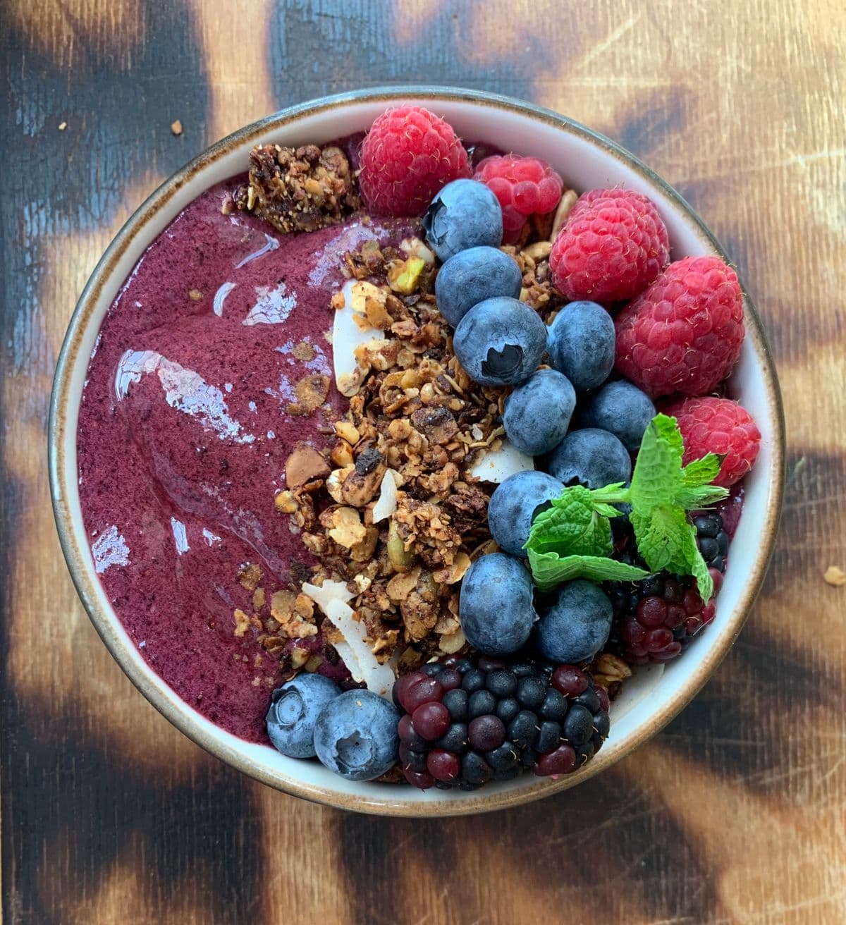 Acai bowl topped with raspberries, blueberries, granola and mint
