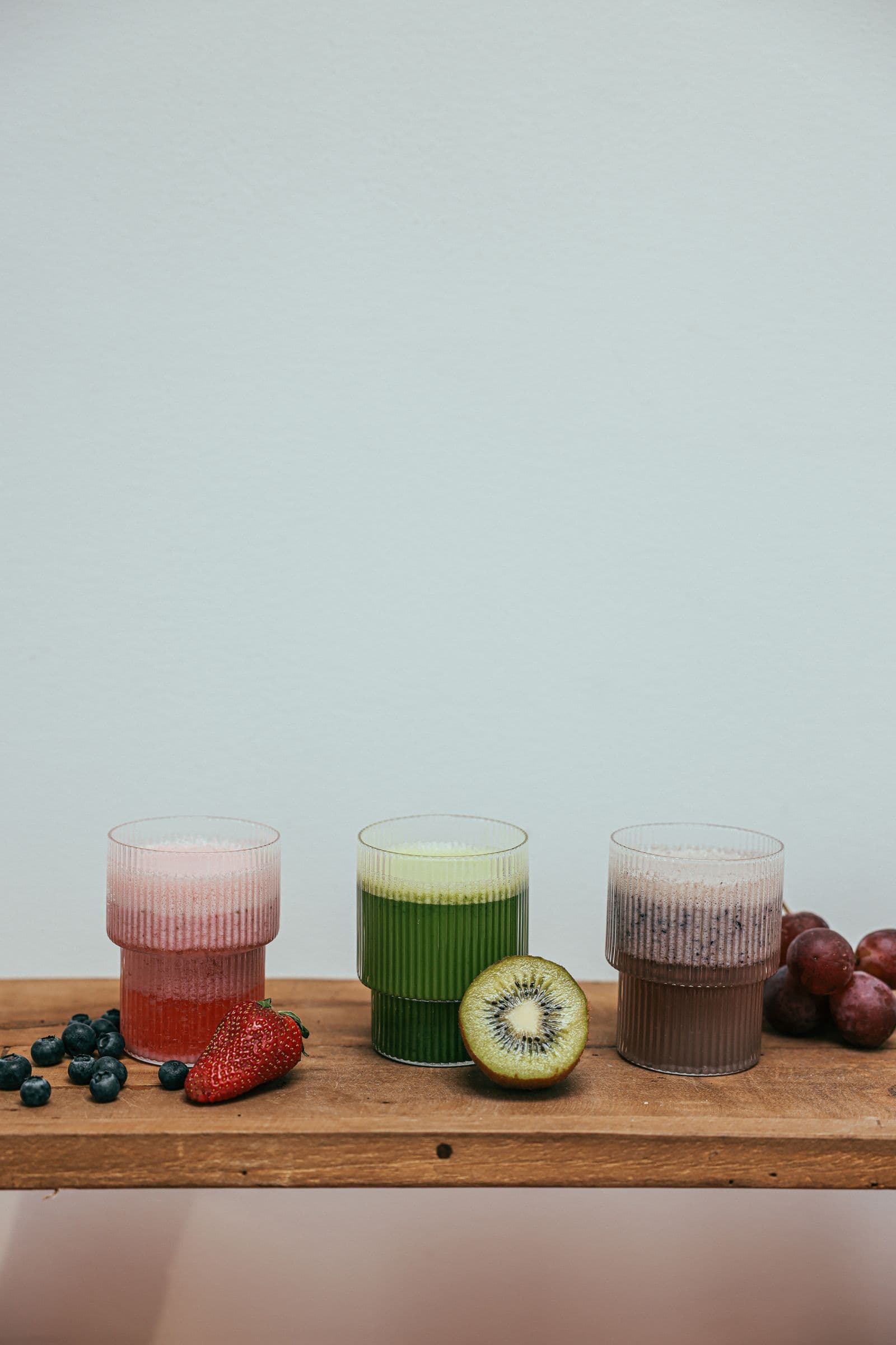Three fruit smoothies with berries and kiwi on a wooden shelf