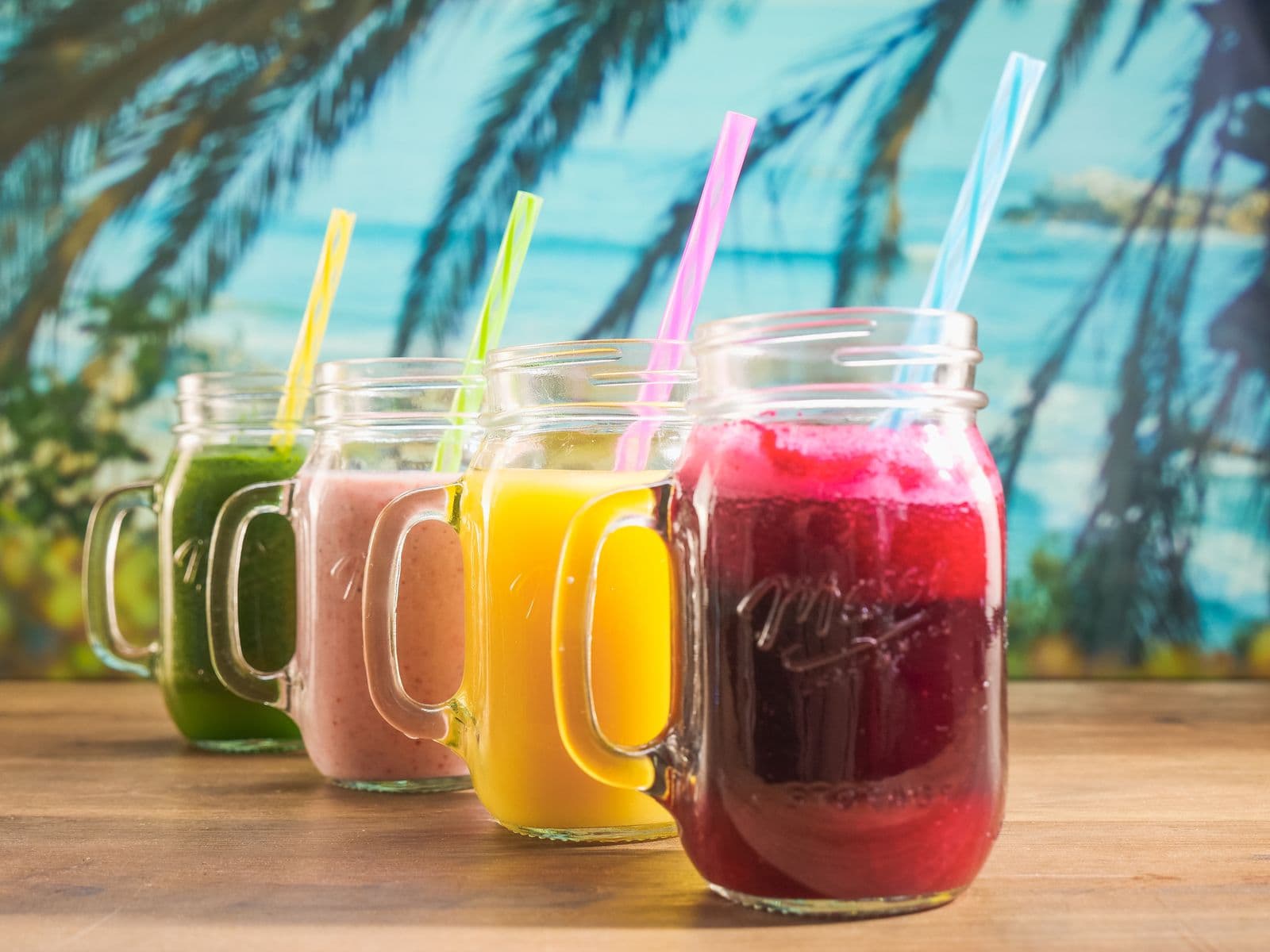Row of colorful smoothies in mason jars, green through orange to deep berry red